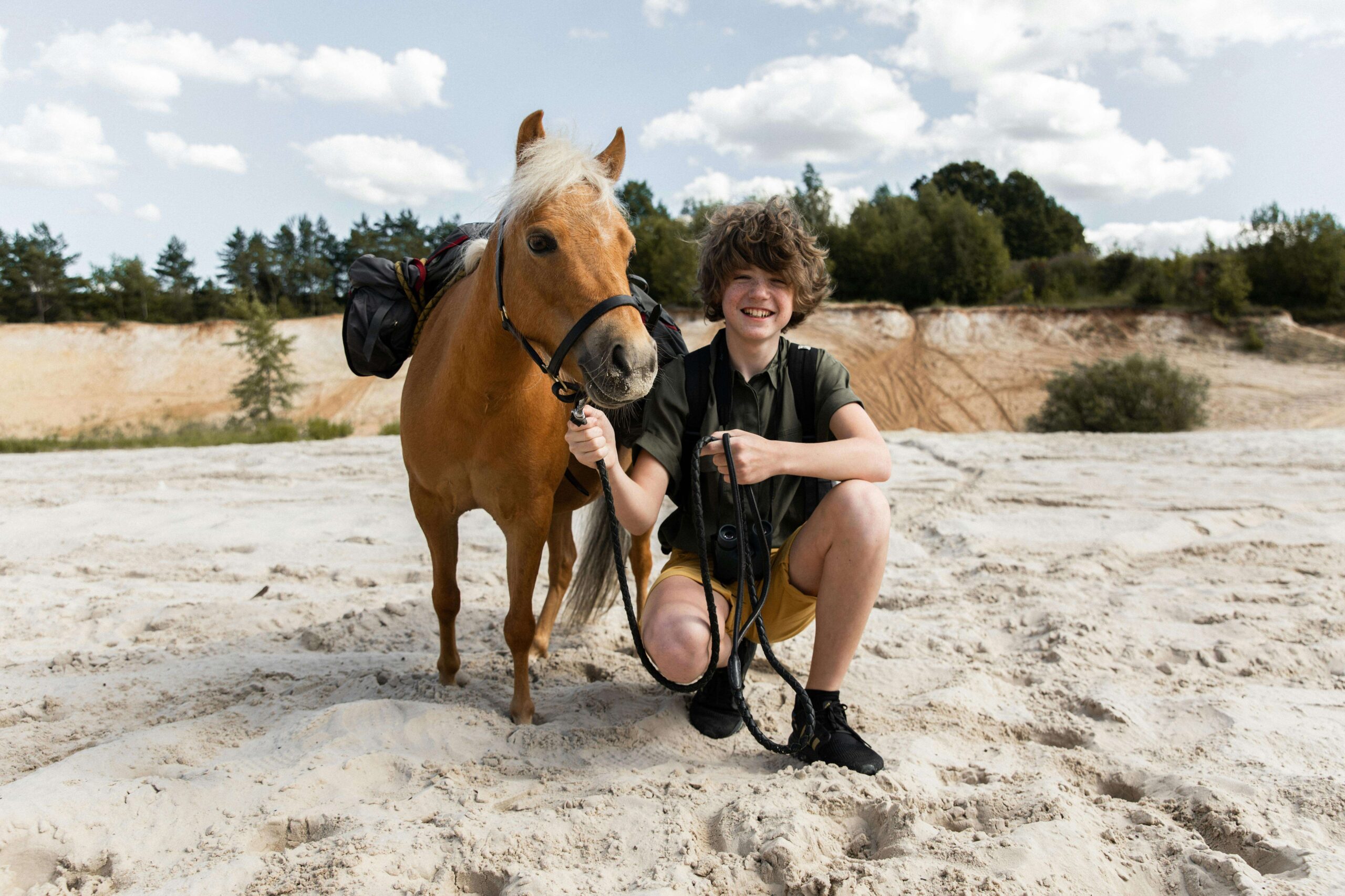 Teenager with a pony enjoying a sunny adventure on a sandy landscape.